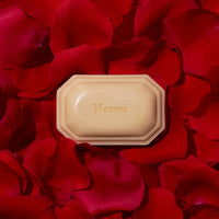 A bar of triple-milled soap from the Caswell Massey Marem Three-Soap Set placed in the center of a backdrop composed of vibrant red rose petals.