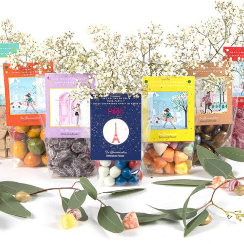 Assorted colorful travel-themed candy packages displayed with Senteurs de France traditional marshmallows and decorative flowers around them.