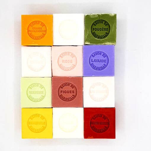 A collection of colorful square Senteurs De France Marseille Bitter Almond soaps neatly aligned in a grid, each labeled with scents such as lavender, rose, and Bitter Almond, against a white background.
