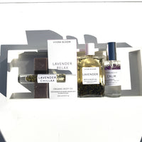 A collection of Hydra Bloom Beauty Lavender-infused wellness products including soap bars, Hydra Bloom Beauty Lavender Chillax Organic Essential Perfume oil roll-on, and bath soak displayed in a white geometric shelf against a white background.