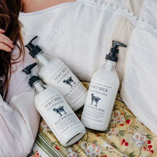 A woman in a white blouse sits with three bottles of Nustad Family Ranch Lavender Sage Goat Milk Lotion on a floral fabric. The bottles are labeled "Fragrance Free" and "Wild Magnolia.
