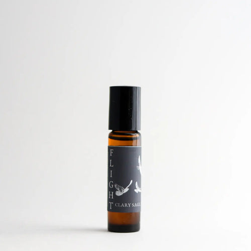 A clear bottle of Nustad Family Ranch Flight Essential Oil Perfume Roller with a black cap, standing against a plain white background. The label features a minimalistic bird design and mentions it contains organic jojoba oil.