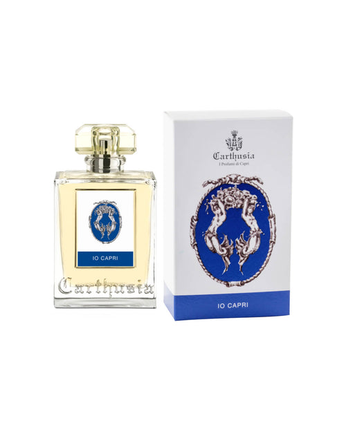 A square perfume bottle labeled "Carthusia Io Capri Eau de Parfum - 100ml" by Carthusia I Profumi de Capri, with a golden cap, next to its ornate blue and white box featuring an intricate crest design incorporating wild fig.