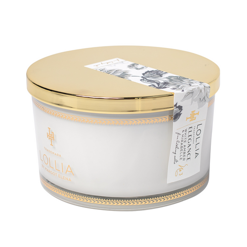 A cylindrical Margot Elena brand candle with "White Amber & Mirabelle" scent in a white and gold container, featuring elegant floral and stripe designs on the label.