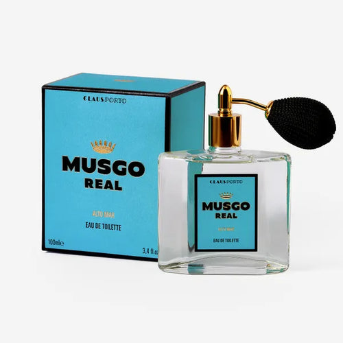 A square glass perfume bottle with a golden spray nozzle and black tassel, beside its turquoise box labeled "Claus Porto Musgo Real Alto Mar Eau de Toilette".