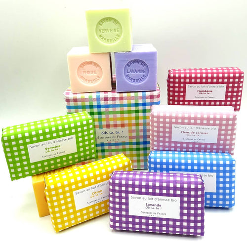 Colorful array of Senteurs De France Vichy Raspberry Soaps in various scents, including organic donkey milk and Vichy Raspberry Soap, packaged in bright polka-dotted and striped boxes, stacked.