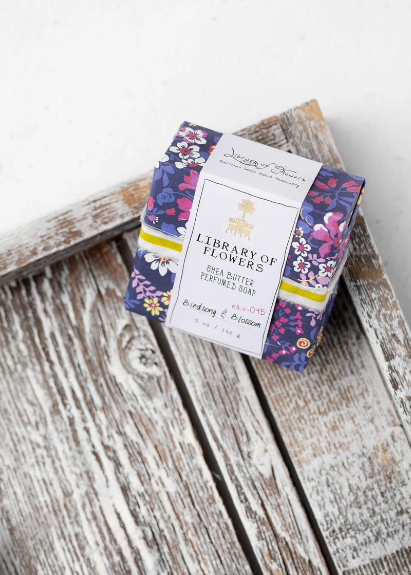 Elegant floral packaging of "Margot Elena Library of Flowers Violet & Pink Roses Square Soap" placed on a rustic wooden chair with a white background.