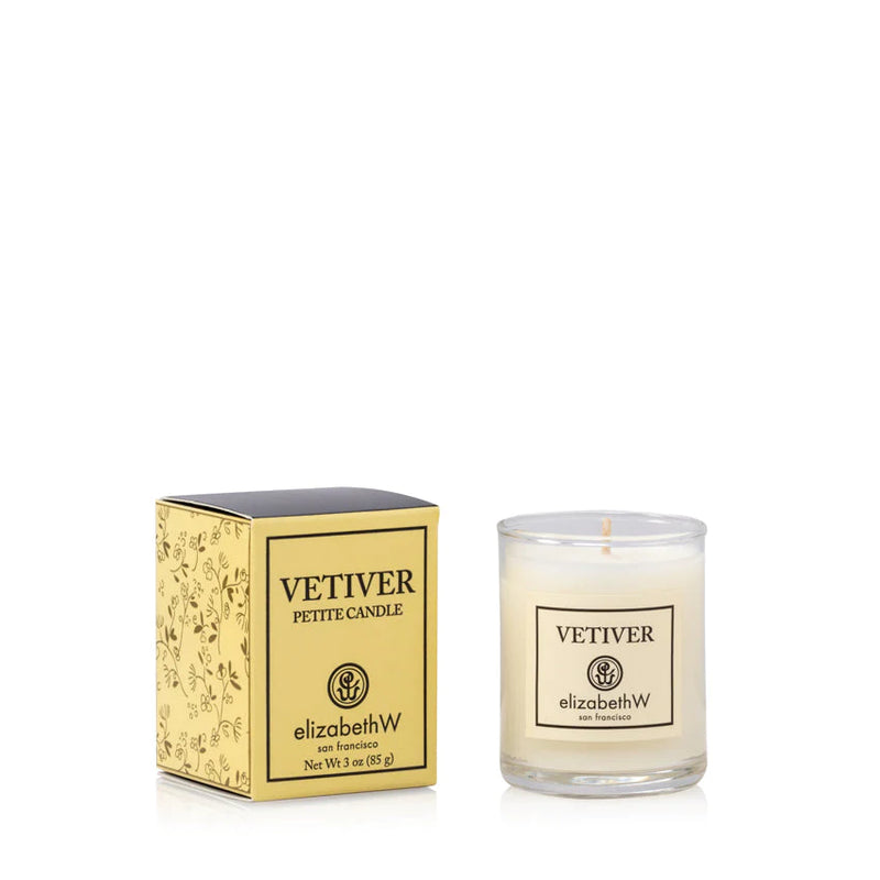 A elizabeth W Vetiver Candle - Petite in a clear glass holder next to its decorative yellow box adorned with floral patterns.