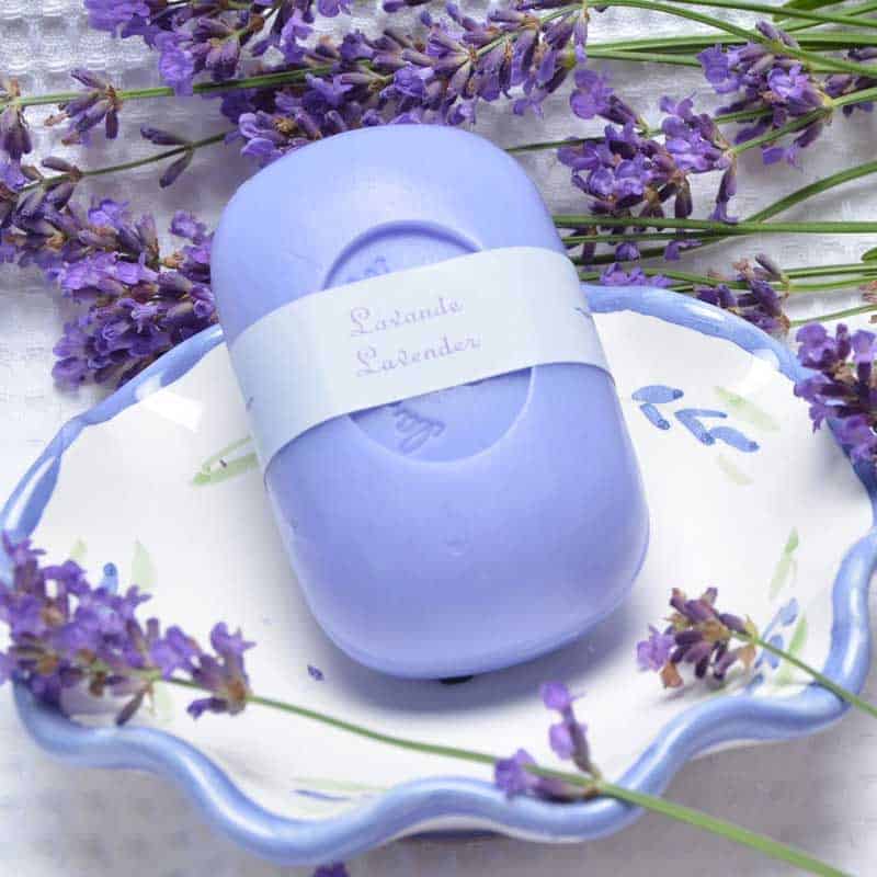 A La Lavande Curved Bar Soap - Lavender soap bar labeled "relaxante lavender" rests on a decorative plate surrounded by fresh lavender sprigs, enhancing its serene and aromatic theme.