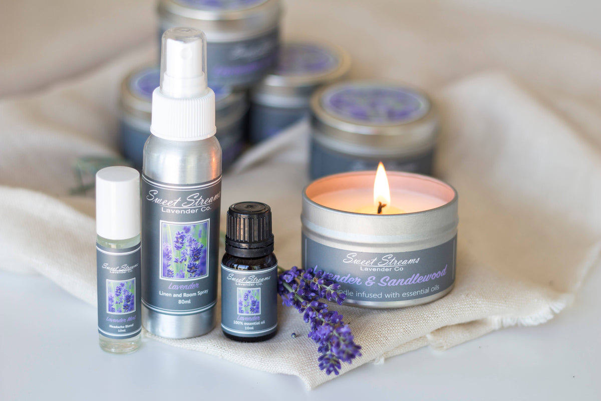 A collection of Sweet Streams Lavender Co. - Lavender Essentials Gift Sets including candles, a Lavender Linen Spray, and essential oils, arranged elegantly on a soft cloth with fresh lavender sprigs.