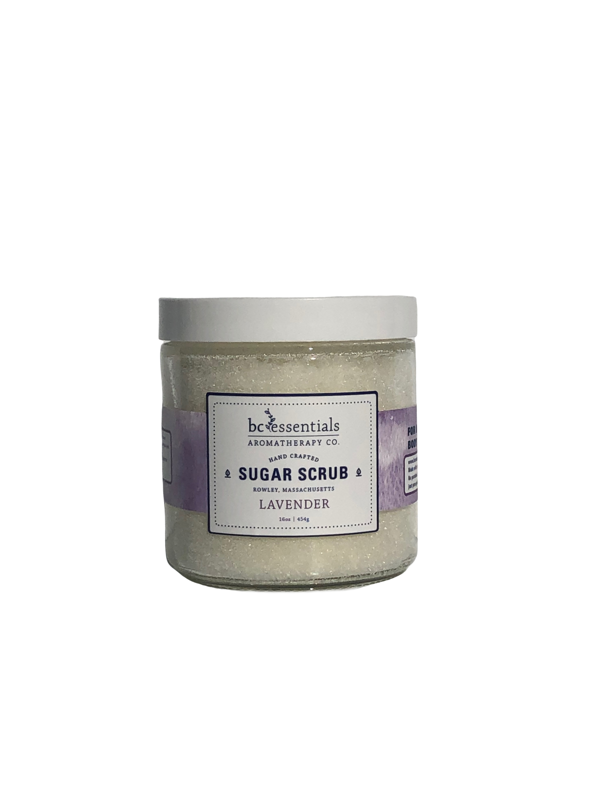 A jar of BC Essentials lavender sugar scrub - 16 oz, against a solid gray background. The jar is clear with a silver cap, displaying the light purple scrub.