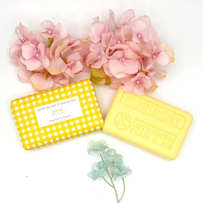 Two bars of Senteurs De France organic luxury soap, one labeled "citron" and the other "savon au lait d'anesse bio," beside a cluster of pink hydrangea flowers.
