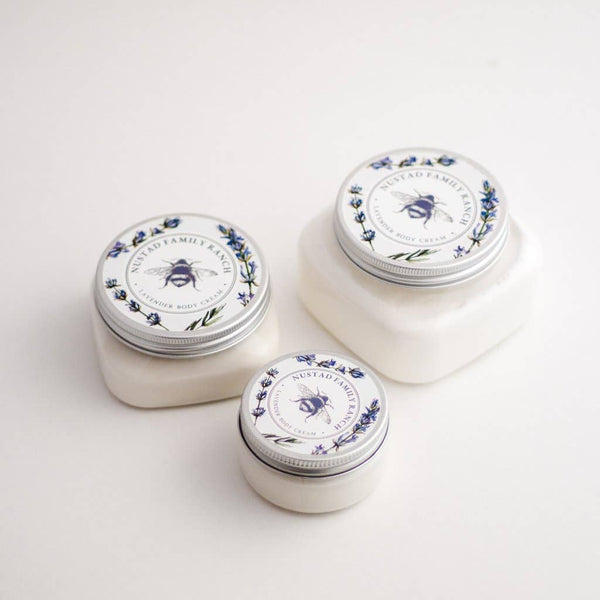 Three small, round jars of Nustad Family Ranch French Lavender Shea Body Butter displayed against a white background, with labels featuring intricate floral designs and highlighting lavender essential oil.