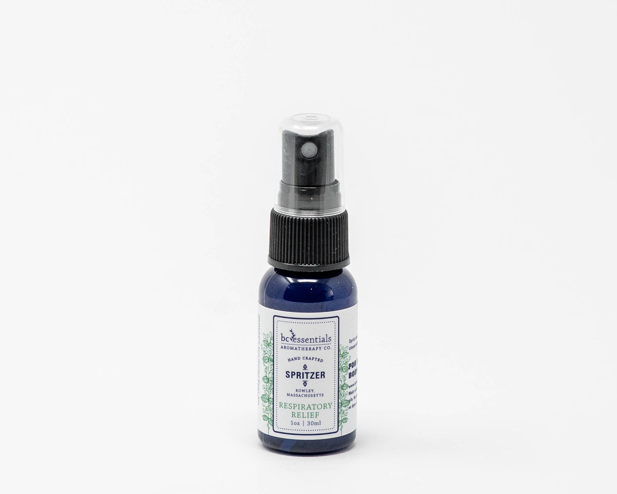 A small blue bottle of BC Essentials eucalyptus essential oil respiratory spritzer with a black spray nozzle, isolated on a white background.