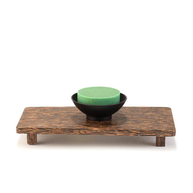 A small Three Sisters Apothecary black metal shave bowl on a dark wooden rectangular serving tray with raised legs, placed against a white background.