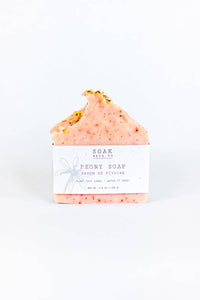 A SOAK Bath Co. - Peony Soap Bar with gold flakes on top, wrapped in plantable seed paper, against a white background. The label features a drawn bow and text describing the product.