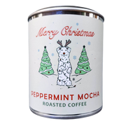 A festive holiday-themed coffee tin labeled "Fox + Hound Christmas Peppermint Mocha Flavored Coffee" featuring a cheerful snowman and green Christmas trees against a white background.