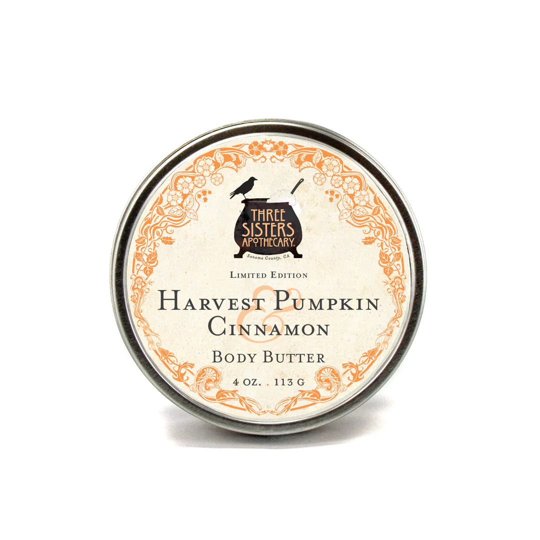 A round tin of Three Sisters Apothecary Harvest Pumpkin & Cinnamon Body Butter labeled "harvest pumpkin cinnamon" in an ornate orange and black design, isolated on a white background.