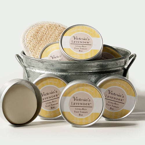 A collection of Victoria's Lavender Lavender Lemonsage foot therapy lotion bars in metal tins, displayed in a rustic gray metal tub with a natural sponge on top.