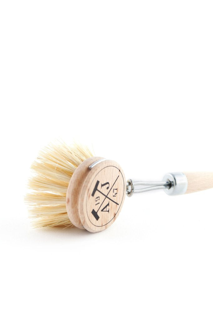 A wooden shaving brush with a silver metallic handle, its bristles fanned out, isolated on a white background. The handle has a circular, wooden end with engraved symbols and is made in France.
