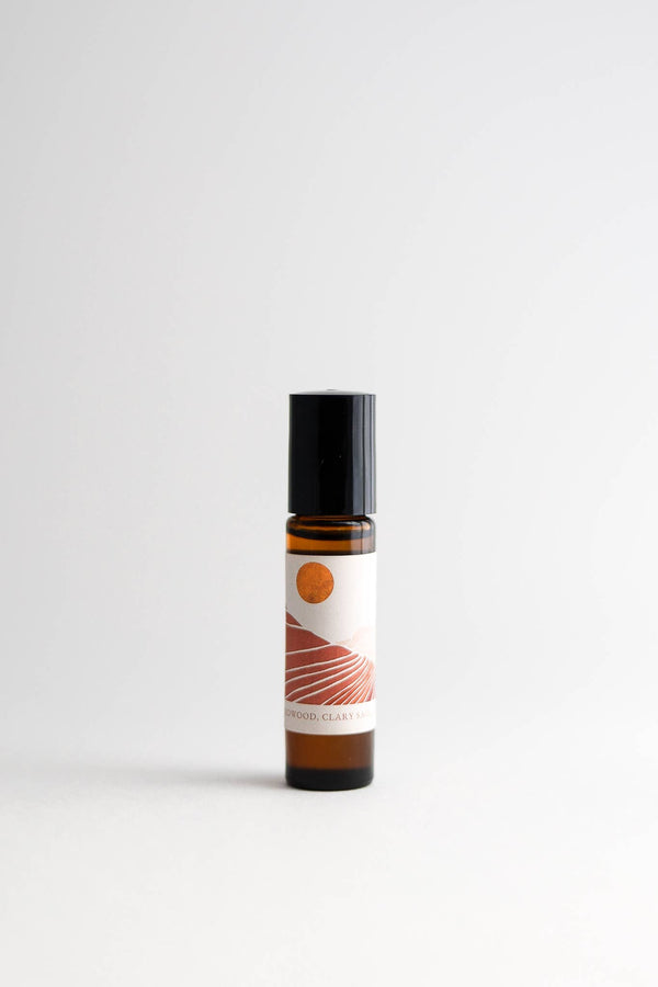 A bottle of Nustad Family Ranch Essential Oil Perfume Roller Golden Hour with a black cap, labeled "sandalwood calary", against a clean, grey background. The label features an abstract orange and white design and includes organic jojoba.
