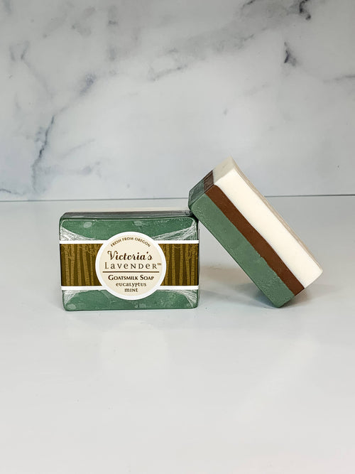 Two bars of Victoria's Lavender's handmade soap, Lavender Eucalyptus Mint and Goat's Milk flavor, displayed upright and flat on a counter with a marble background.