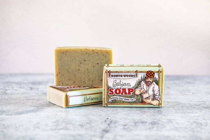 A bar of Primitive House Farm balsam soap beside its vintage-styled packaging featuring an illustration of a man in a checkered shirt and hat, labeled "Maine woods balsam soap.