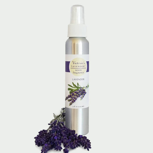 A spray bottle of Victoria's Lavender - Lavender Room Fragrance labeled lavender, with a bunch of purple lavender flowers lying in front of it on a white background.