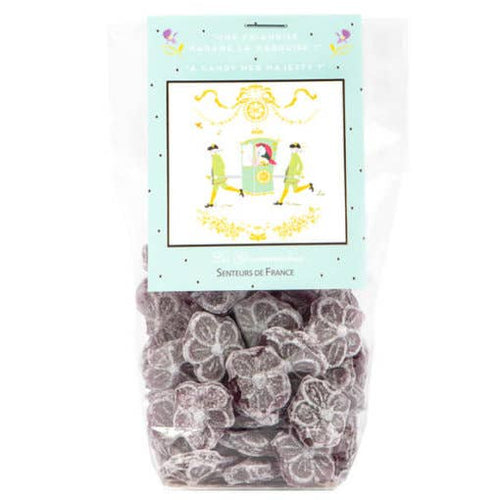 A clear plastic bag filled with gray flower-shaped candies, labeled "Versailles Violettes Candies" in French, featuring a vintage-style botanical illustration of violet flowers on the package, reminiscent of traditional Senteurs De France confectionery.