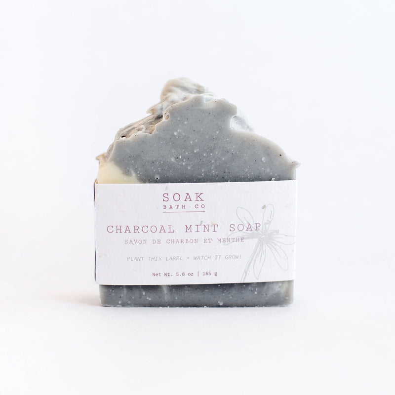 A bar of SOAK Bath Co. - Charcoal Mint Soap with a textured top, wrapped in a minimalist label from "SOAK bath co.," isolated on a white background.