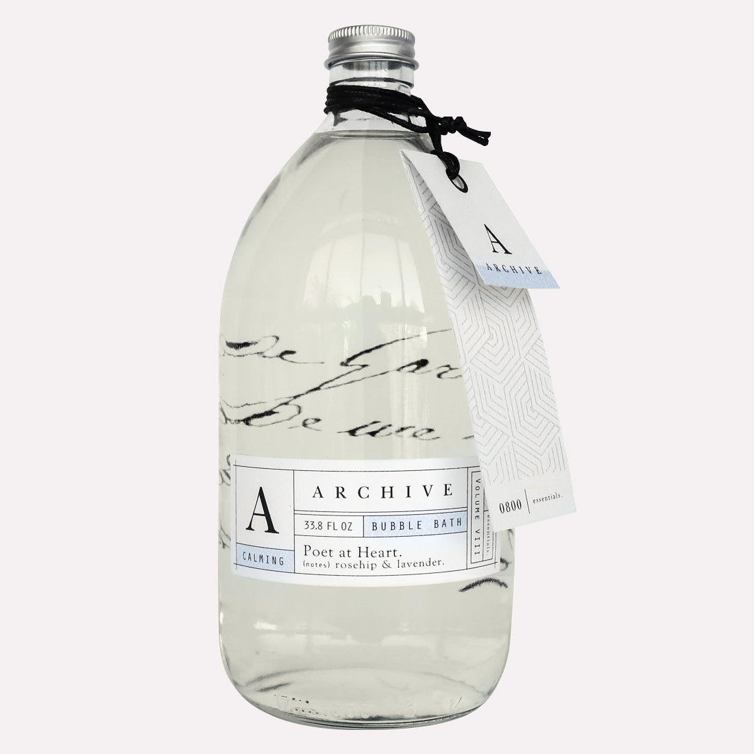 Clear glass bottle of Archive by Margot Elena Poet at Heart Bubble Bath with elegant labeling, filled with a transparent liquid and sealed with a black cap, accompanied by a hanging white tag.
