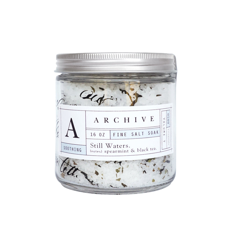 A Margot Elena glass jar of ARCHIVE Still Waters Salt Soak labeled "16 oz, Spearmint & Black Tea." The jar reveals visible salt crystals and purifying minerals with a clean, minimalist design.