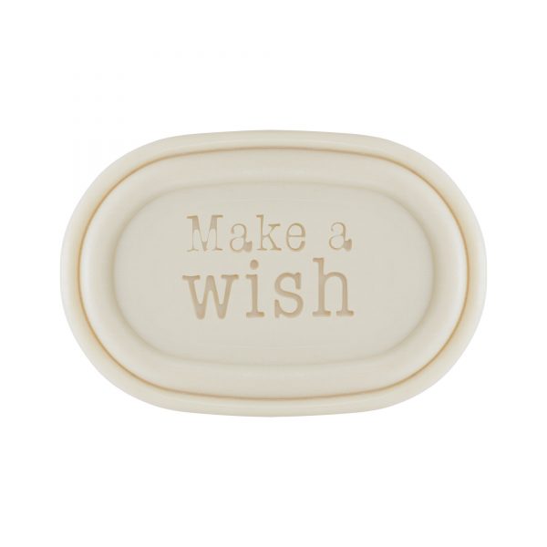 A simple oval-shaped, cream-colored ceramic dish with the phrase "make a wish" embossed in a gentle, serif font in the center, inspired by vintage soap box design, reminiscent of Victloria Scandinavian Merry Christmas Soap - Sledding Boy.