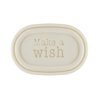 A simple oval-shaped, cream-colored ceramic dish with the phrase "make a wish" embossed in a gentle, serif font in the center, inspired by vintage soap box design, reminiscent of Victloria Scandinavian Merry Christmas Soap - Sledding Boy.