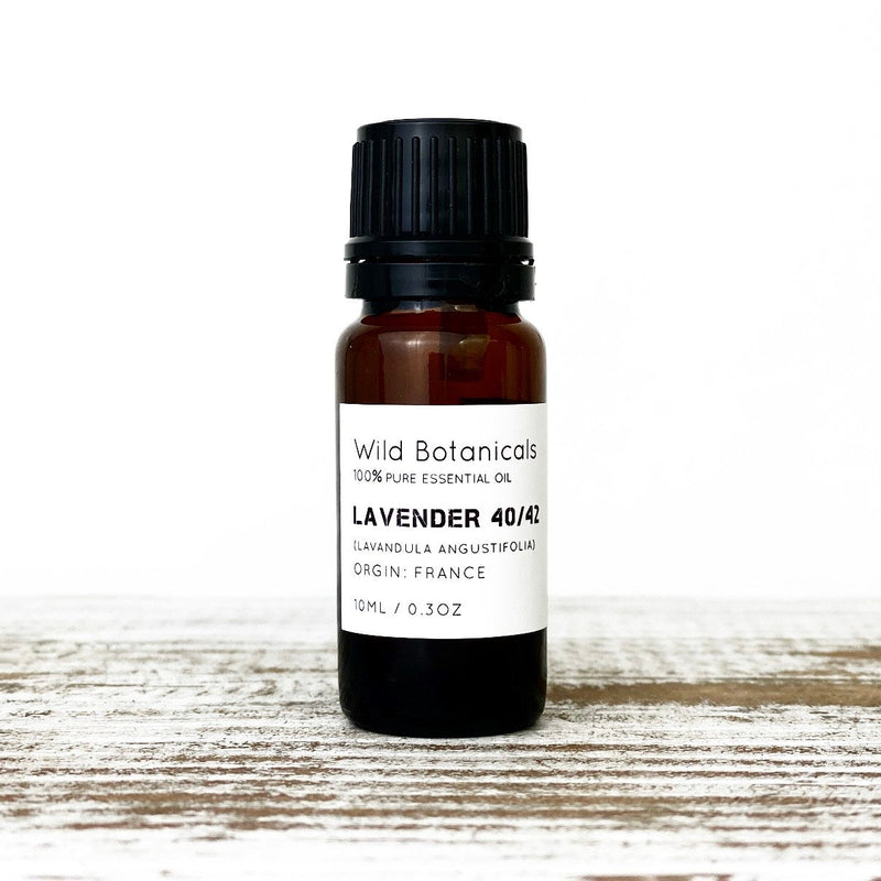 A bottle of Wild Botanicals Lavender Essential Oil labeled with details about its purity and origin in France, placed on a white wooden surface.