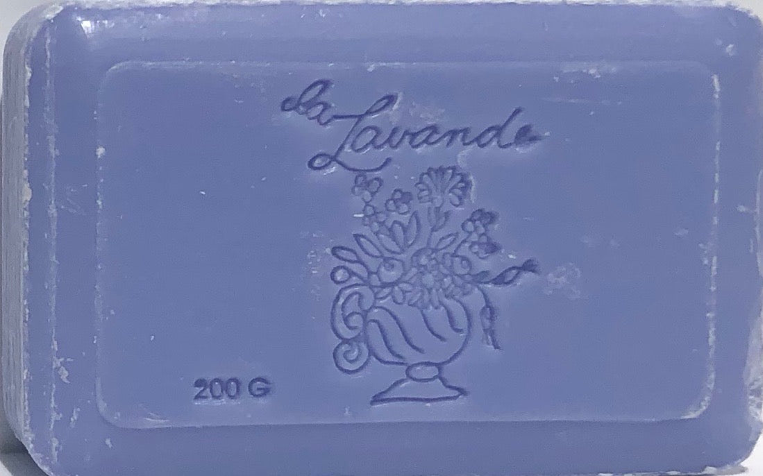 A La Lavande Lavender Blue Soap bar with the embossed inscription "la lavande" and a decorative floral design, featuring various flowers in a vase. The soap, infused with Shea Butter, weighs 200 grams.