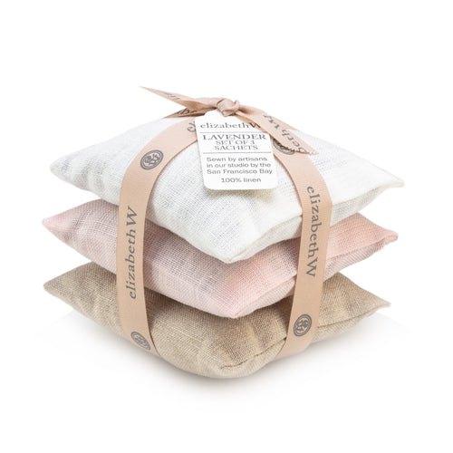 Three stacked elizabeth W Lavender Sachet Set of 3 Ivory, Natural, Pink Linen sachets with the label "elizabeth w French lavender sachets," tied together with a ribbon, isolated on a white background.