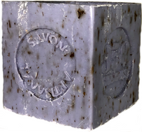 A close-up image of a worn, purple La Lavande Cube Lavender Flower soap bar with embossed text and logo details, showing signs of use and small embedded particles.