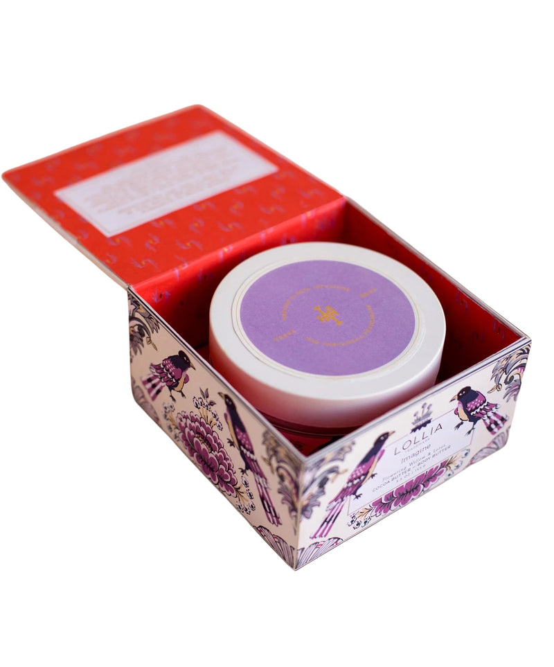 A decorative purple and red box with intricate floral patterning, partially open to reveal a round container of Margot Elena's Lollia Imagine Body Butter with a lavender-colored lid featuring a golden design.