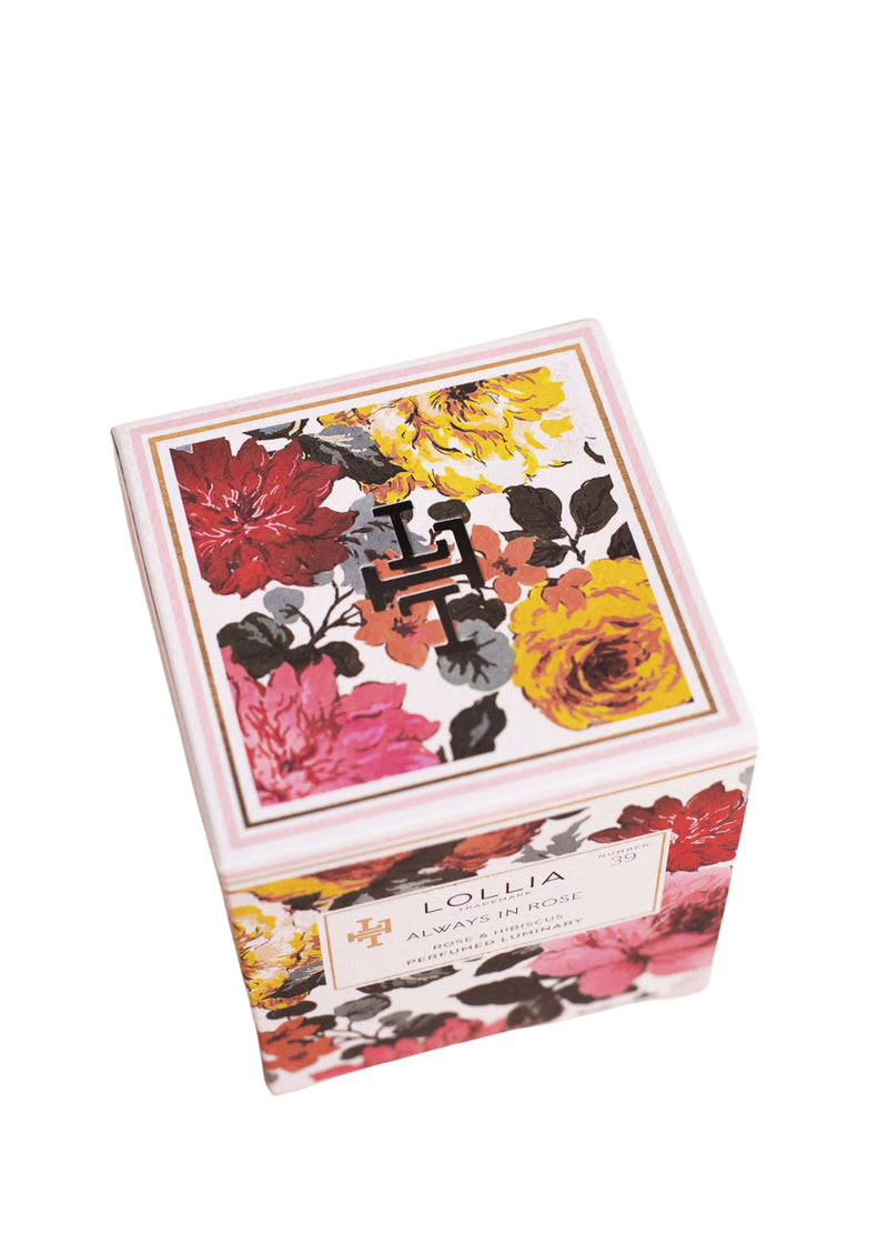 A square Lollia Always in Rose No. 39 Perfumed Luminary Candle box decorated with colorful floral prints in red, yellow, and dark shades, featuring a modern monogrammed candle, isolated on a white background by Margot Elena.