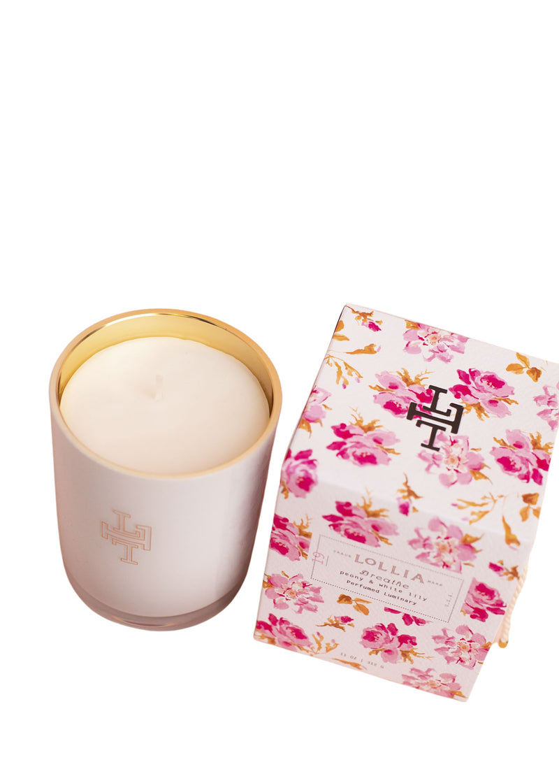 A Lollia Breathe No. 19 Luminary Candle in a white container with a gold rim, made from a soy wax coconut wax blend, beside its floral-patterned packaging branded "Margot Elena" on a white background.