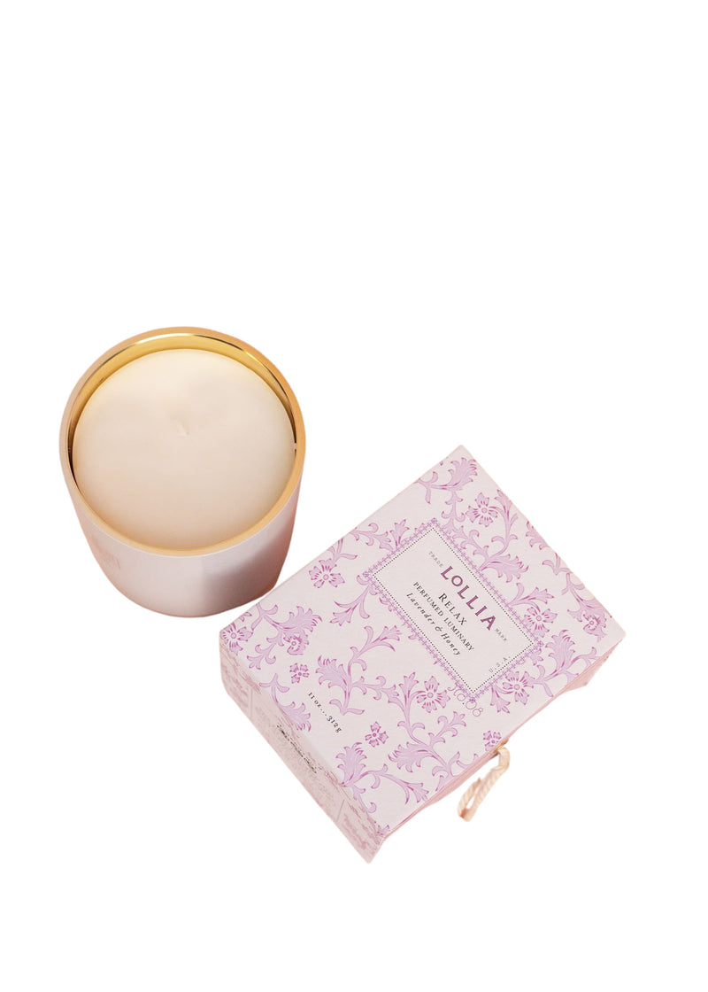 A Lollia Relax No. 08 Luminary Candle in a gold-rimmed glass container next to its pink and white floral-patterned packaging box with the brand name "Margot Elena" visible.