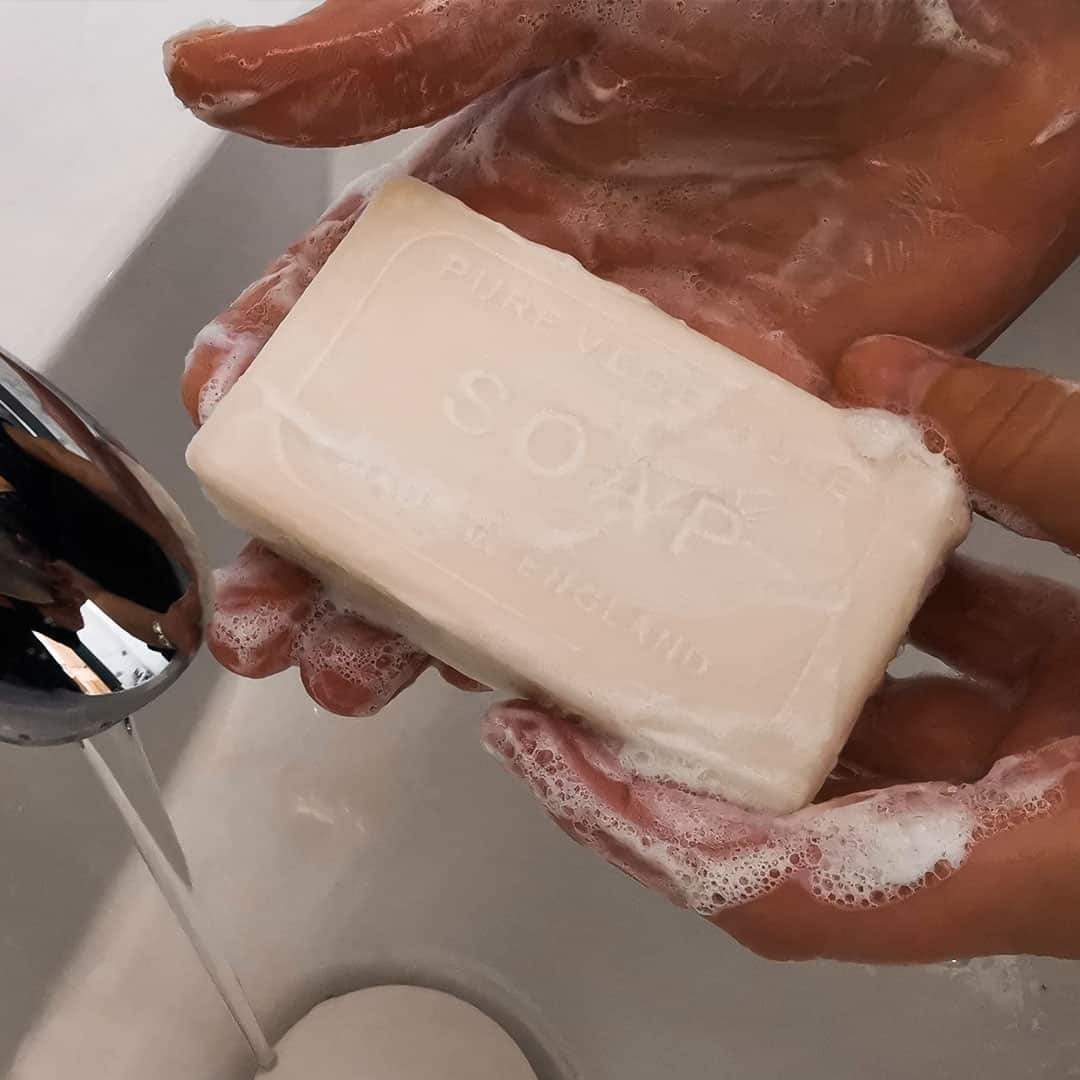 Hands washing with a bar of The English Soap Co. Vintage Rose Vintage Italian Wrapped Soap under running water from a faucet, creating foam, emphasizing cleanliness and hygiene.
