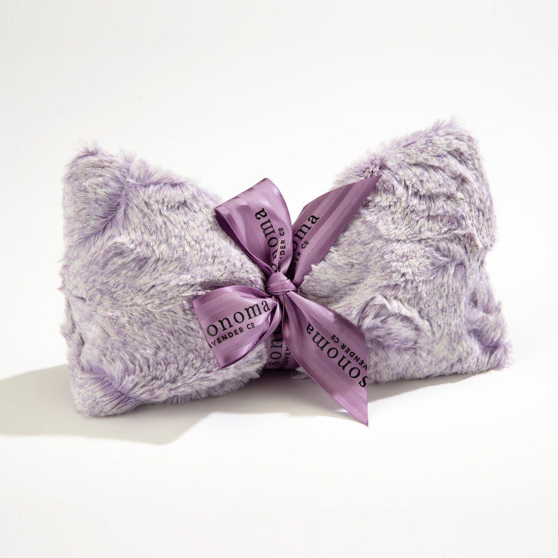 A plush, lavender-colored faux fur throw pillow tied with a silky purple ribbon printed with "Sonoma Lavender Aster Heather Spa Mask" in a repeating pattern, against a white background.