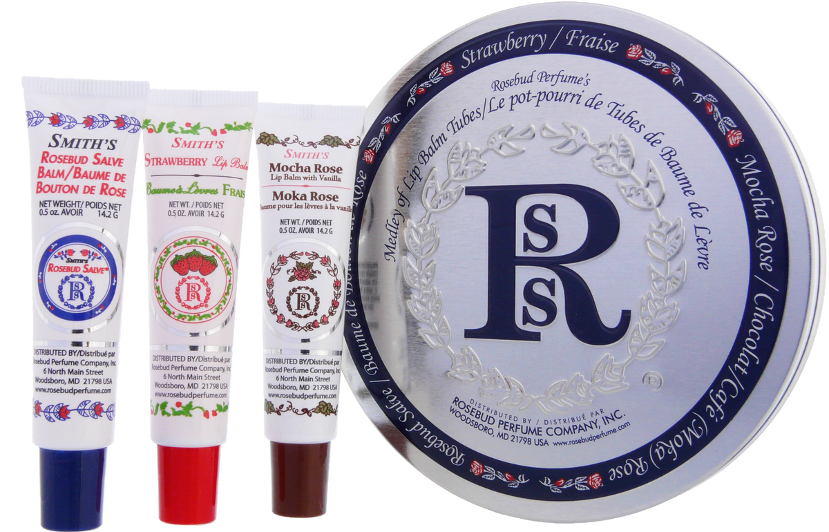An arrangement of four Rosebud Perfume Co.'s Smith’s Medley of Lip Balm Tubes displayed in front of their circular tin package, featuring flavors including Rosebud Salve Tube and strawberry, mocha rose, and minted rose.