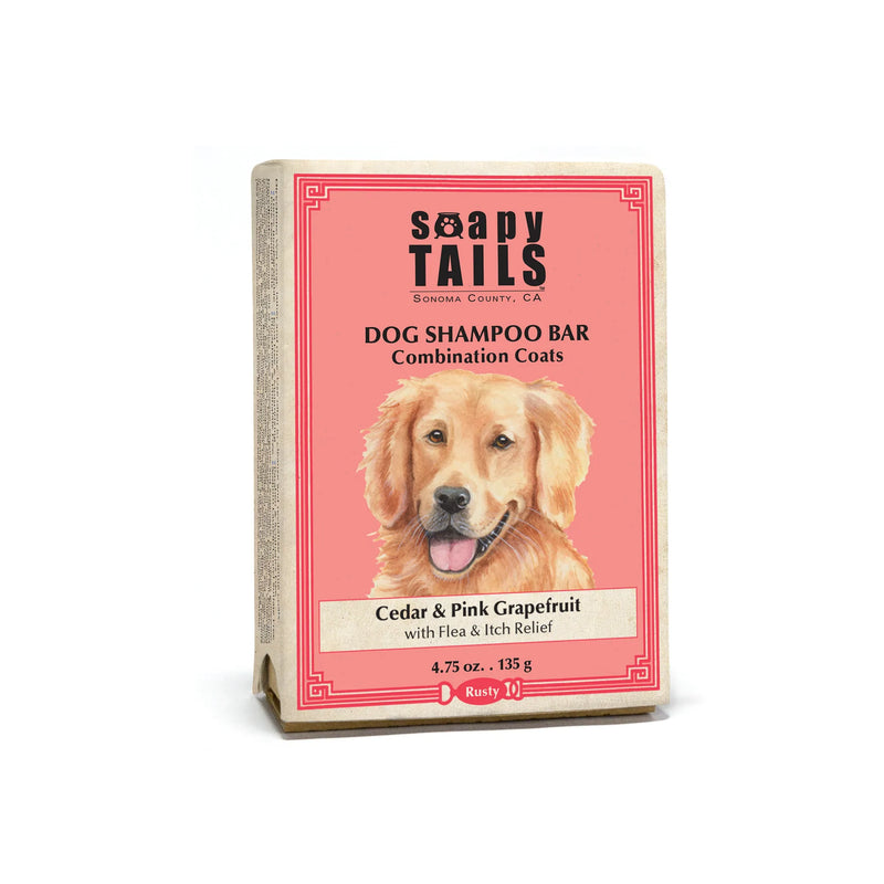 A Three Sisters Aphothecary dog shampoo bar packaging labeled "Soapy Tails" with an image of a golden retriever on the front. The package features cedar and pink grapefruit scent details and highlights its "Healthy Coat" formula.