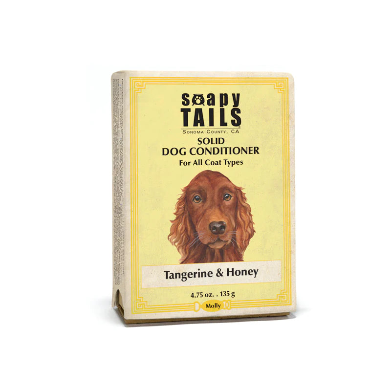 A solid dog conditioner product called "Soapy Tails Solid Conditioner Bar - All Coat Types" from Three Sisters Apothecary in Sonoma County, CA, packaged in a yellow box featuring an illustration of a brown dog. Text indicates "Tangerine & Honey.