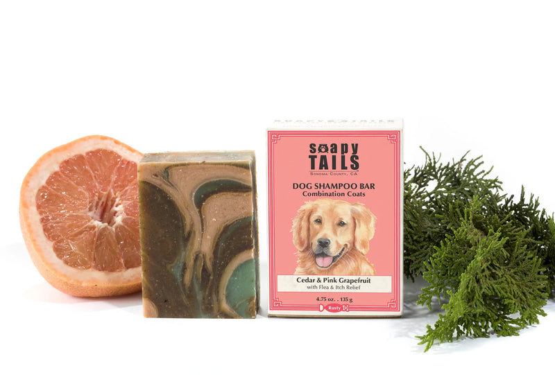 A Soapy Tails Shampoo Bar - Cedar & Pink Grapefruit - Combination Coats by Three Sisters Aphothecary, with a golden retriever on the package, next to a slice of grapefruit and a sprig of greenery, on a white background.