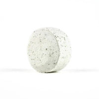 A single speckled grey round stone, reminiscent of a Spinster Sisters Eucalyptus Shower Steamer, placed against a clean, white background.