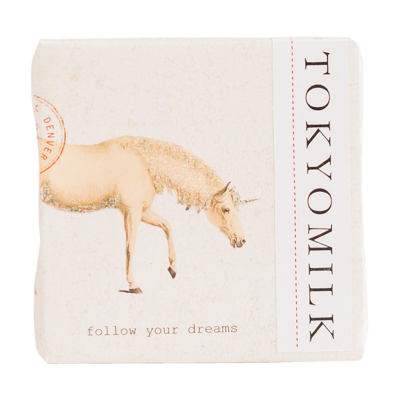 A square notebook with a vintage beige background, featuring a glittery golden unicorn and the words "follow your dreams" alongside vertical text "Margot Elena TokyoMilk Finest Perfumed Soap - Follow Your Dreams.